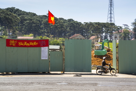 DALAT, VIETNAM - FEBRUARY 10: Man on motorbike in front of construction site with excavator and Vietnamese flag on February 10, 2012 in Dalat, Vietnam.のeditorial素材
