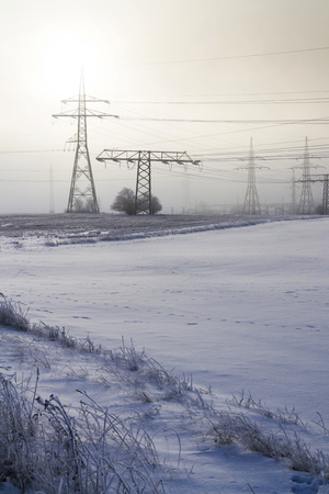 Electricity pylons from distribution power station in foggy winter freezeの写真素材