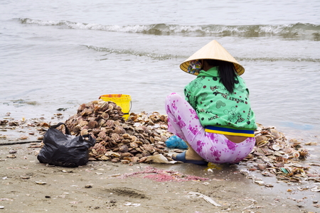MUI NE, VIETNAM - FEBRUARY 7: Women processing seashells with fishing boats in background on February 7, 2012 in Mui Ne, Vietnam.のeditorial素材