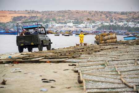 MUI NE, VIETNAM - FEBRUARY 7: Fishermen driving car on beach with colorful fishing boats on February 7, 2012 in Mui Ne, Vietnam.のeditorial素材