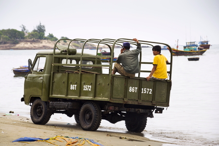 MUI NE, VIETNAM - FEBRUARY 7: Fishermen driving car on beach with colorful fishing boats on February 7, 2012 in Mui Ne, Vietnam.のeditorial素材