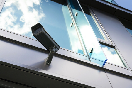 Grey security camera with window reflecting blue sky clouds