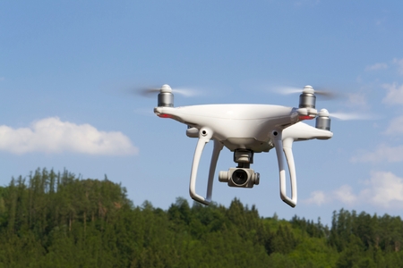 White drone quadrocopter with camera flying over forestの写真素材