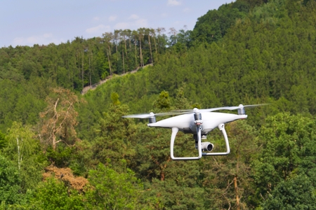 White drone quadrocopter with camera flying over forestの写真素材