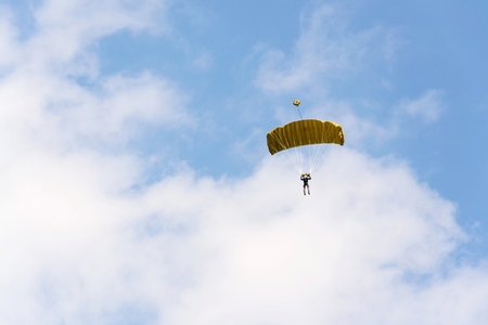 Parachutist skydiving with open yellow parachute clouds blue sky backgroundの写真素材