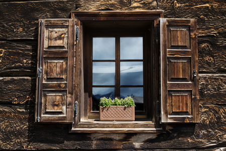 Beautiful open wooden window shutter with flowers reflecting blue skyの写真素材