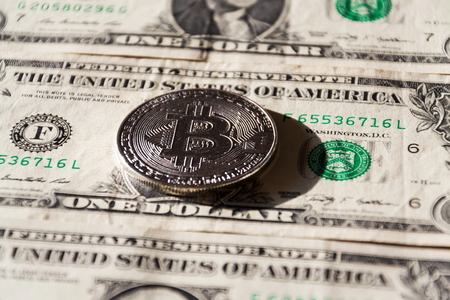 Silver bitcoin coin lying on United States dollars, cryptocurrency concept