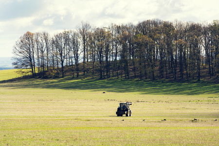 Tractor riding on meadow with forest background, food self-sufficiency concept