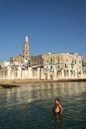 MONOPOLI, ITALY - JULY 2 2018: People swimming on beach Porta Vecchia near Cathedral during sunrise on July 2, 2018 in Monopoli, Italy.のeditorial素材
