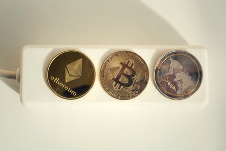 Bitcoin, Ethereum and Ripple coins lying on power strip extension cord with 3 sockets, largest cryptocurrencies by market capitalization, cryptocurrency investing, energy consumption and footprint conceptの写真素材