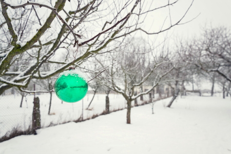 Green Christmas ball vintage glass decoration hanging on tree outdoors, falling snow winter landscape backgroundの写真素材