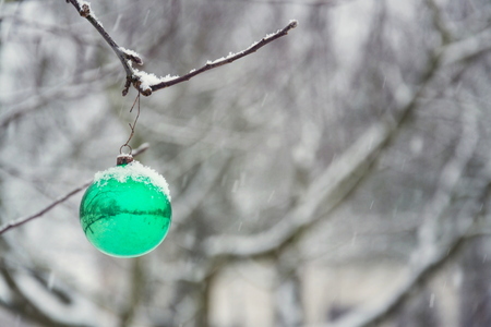 Green Christmas ball vintage glass decoration hanging on tree outdoors, falling snow winter landscape backgroundの写真素材