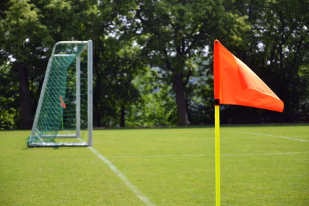 Orange vivid corner flag on fresh green football ground, trees in background, sunny summer day