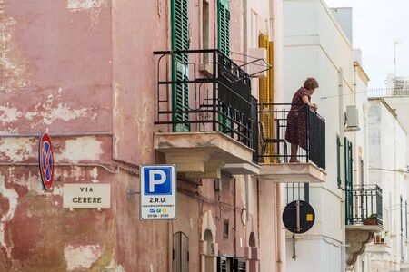 POLIGNANO A MARE, ITALY - JULY 6 2018: Older local woman looking to street from balcony on July 6, 2018 in Polignano a Mare, Italy.のeditorial素材