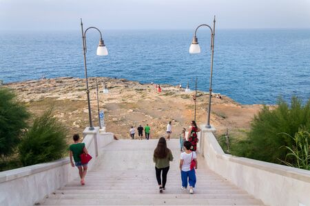 POLIGNANO A MARE, ITALY - JULY 6 2018: Tourist on stairs leading to dramatic cliffs over Adriatic sea beside beach Lama Monachile on July 6, 2018 in Polignano a Mare, Italy.のeditorial素材