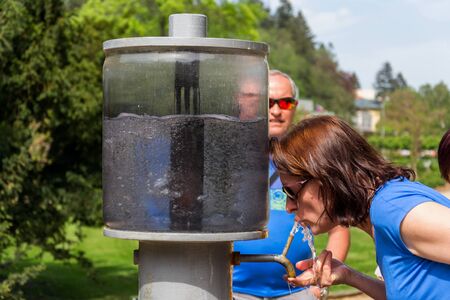 LUHACOVICE, CZECH REPUBLIC - APRIL 30 2018: People drinking from public natural healing mineral stream with mineralized water in spa town on April 30, 2018 in Luhacovice, Czech Republic.のeditorial素材