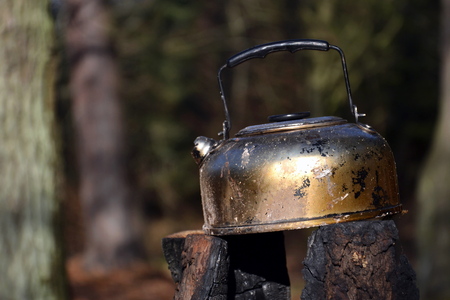 Tin tea kettle stands on spent swedish fire torch in forest, fallen leaves nature background, sunny autumn dayの写真素材
