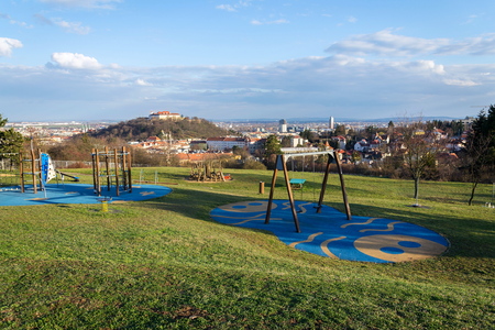 Beautiful playground with wooden swing and climbing frames for children with Spilberk castle in background, Brno, Moravia, Czech Republic, sunny dayの写真素材