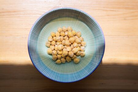 Chickpeas soaked in bowl with water before cooking to shorten cooking time, wooden table backgroundの写真素材