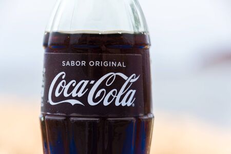 EL MEDANO, SPAIN - JULY 10 2019: Coca-Cola company logo on glass bottle with Coke with sea in background on July 10, 2019 in El Medano, Spain.のeditorial素材