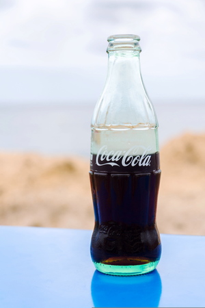 EL MEDANO, SPAIN - JULY 10 2019: Coca-Cola company logo on glass bottle with Coke with sea in...