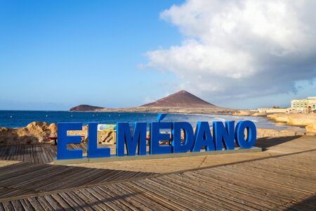 Three-dimensional sign El Medano on long promenade along the coast and beach  with Montana Roja in the background, El Medano, Tenerife, Canary Islands, Spain, sunrise on sunny summer dayの写真素材