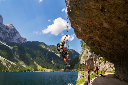 GOSAU, AUSTRIA - JULY 4 2019: Man climbing on Laserer alpin via ferrata over Vorderer Gosausee lake with Grosser Donnerkogel Mountain in background on July 4, 2019 in Gosau, Austria.のeditorial素材
