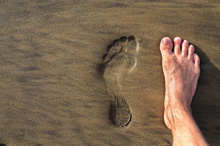Human footprint with barefoot feet in brown yellow sand beach background, active healthy living and...