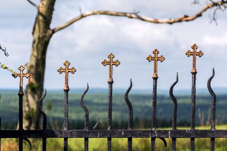 Beautiful small iron crossed fence decoration, graveyard wall with green woods in background, life and death conceptの写真素材