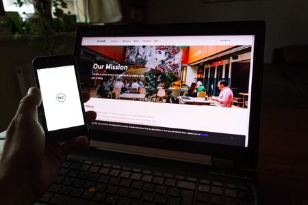 PRAGUE, CZECH REPUBLIC - DECEMBER 19 2019: WeWork commercial real estate company app on phone screen with internet page in background on December 19, 2019 in Prague, Czech Republic.の写真素材