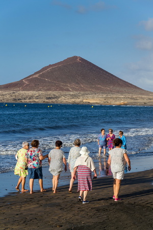 EL MEDANO, SPAIN - JULY 9 2019: Senior local women walking on Playa El Medano beach during sunrisee on July 9, 2019 in El Medano, Spain.のeditorial素材
