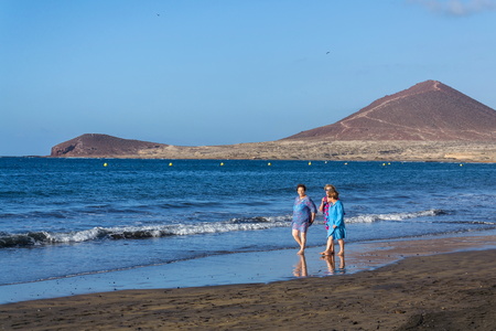 EL MEDANO, SPAIN - JULY 9 2019: Senior local women walking on Playa El Medano beach during sunrisee on July 9, 2019 in El Medano, Spain.のeditorial素材