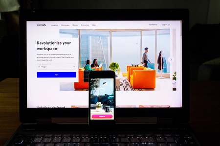 PRAGUE, CZECH REPUBLIC - DECEMBER 19 2019: WeWork commercial real estate company app on phone screen with internet page in background on December 19, 2019 in Prague, Czech Republic.のeditorial素材