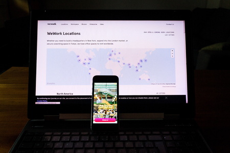 PRAGUE, CZECH REPUBLIC - DECEMBER 19 2019: WeWork commercial real estate company app on phone screen with internet page in background on December 19, 2019 in Prague, Czech Republic.のeditorial素材