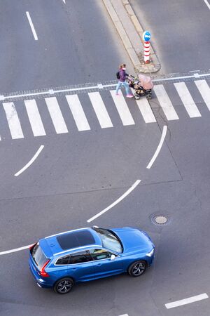 Blue car heading to pedestrian crossing with unrecognizable young woman pushing baby carriage, safety of self-driving autonomous technology concept, aerial birds eye viewの写真素材