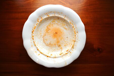 Empty white porcelain plate with finished food leftovers from soup or sauce lays on wooden table, flat lay top viewの写真素材