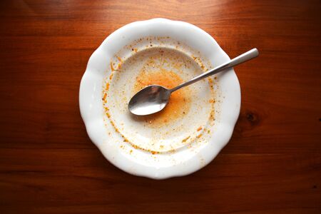 Empty white plate with spoon on wooden table, flat lay top view, red leftovers from soup or sauceの写真素材