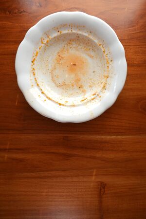 Empty white porcelain plate with finished food leftovers from soup or sauce lays on wooden table, flat lay top viewの写真素材
