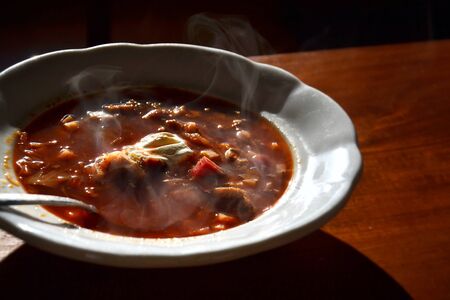 Plateful of hot borscht soup with beetroots, beef, pork, cabbage and carrots, sour cream on top, wooden table backgroundの写真素材