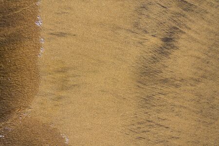 Wawes coming and leaving wet sand on sea shore, brown yellow and black grains from volcanic ash, zen background, harmony and meditation concept, flat lay top view, copy spaceの写真素材