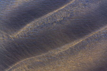 Wawes coming and leaving wet sand on sea shore, brown yellow and black grains from volcanic ash, zen background, harmony and meditation concept, flat lay top view, copy spaceの写真素材