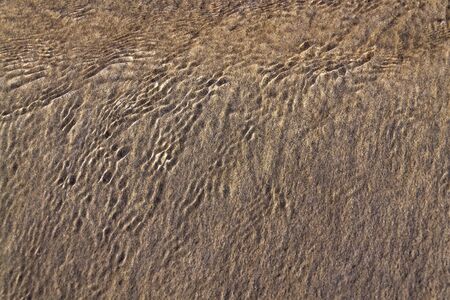 Wawes coming and leaving wet sand on sea shore, brown yellow and black grains from volcanic ash, zen background, harmony and meditation concept, flat lay top view, copy spaceの写真素材
