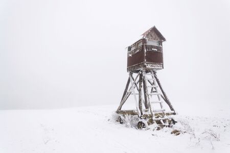 Deer stand, wooden hunters high seat hide on snow covered field, winter foggy dayの写真素材