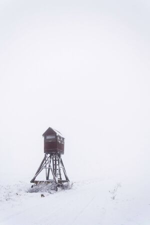 Deer stand, wooden hunters high seat hide on snow covered field, winter foggy dayの写真素材