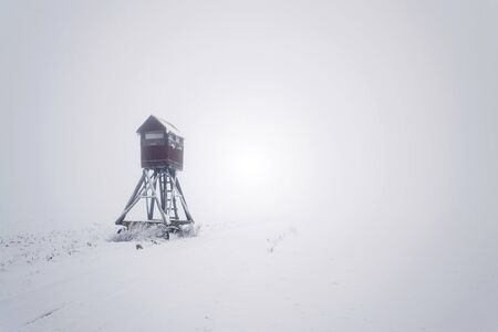 Deer stand, wooden hunters high seat hide on snow covered field, winter foggy dayの写真素材