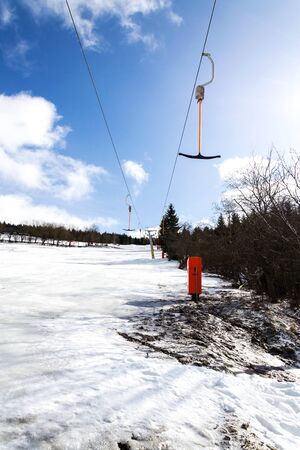 Stopped t-bar surface lift on empty piste, end of ski season concept, slope with disappearing snow, sunny winter or spring dayの写真素材