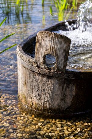 Wooden bucket with oxygenating flowing water at natural swimming pond or pool purifying water without chemicals through biological filters and plantsの写真素材