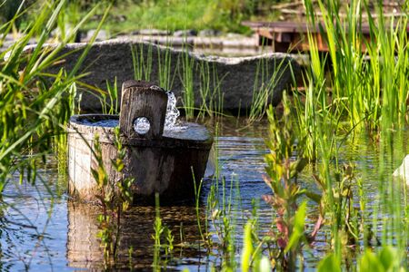 Wooden bucket with oxygenating flowing water at natural swimming pond or pool purifying water without chemicals through biological filters and plantsの写真素材