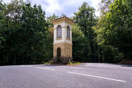 Solitary chapel on crossroad in middle of beautiful woods, road traffic, loneliness or coronavirus quarantine concept, sunny dayの写真素材