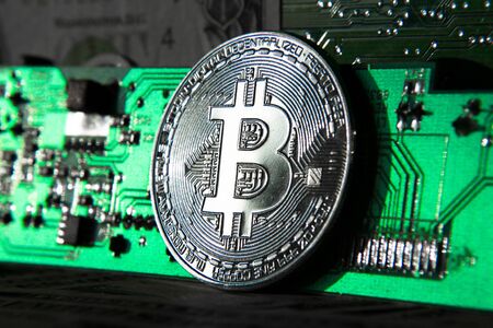 Silver bitcoin coin in front of computer motherboard, cryptocurrency mining and investing conceptの写真素材